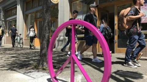 People walk by a hot pink peace sign sculpture in Berkeley